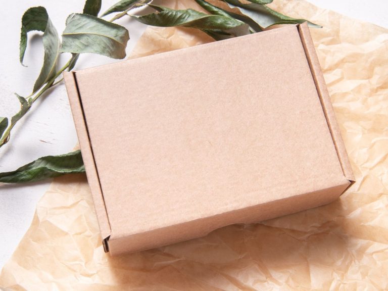 Geschenk Paket Braune Versandbox auf crinkly Papier, umgeben von grünen Blättern.