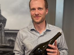 Maximilian Wagner - Sektmanufaktur Wagner Mann in Hemd hält eine große Flasche in der Hand. Hintergrund unscharf.